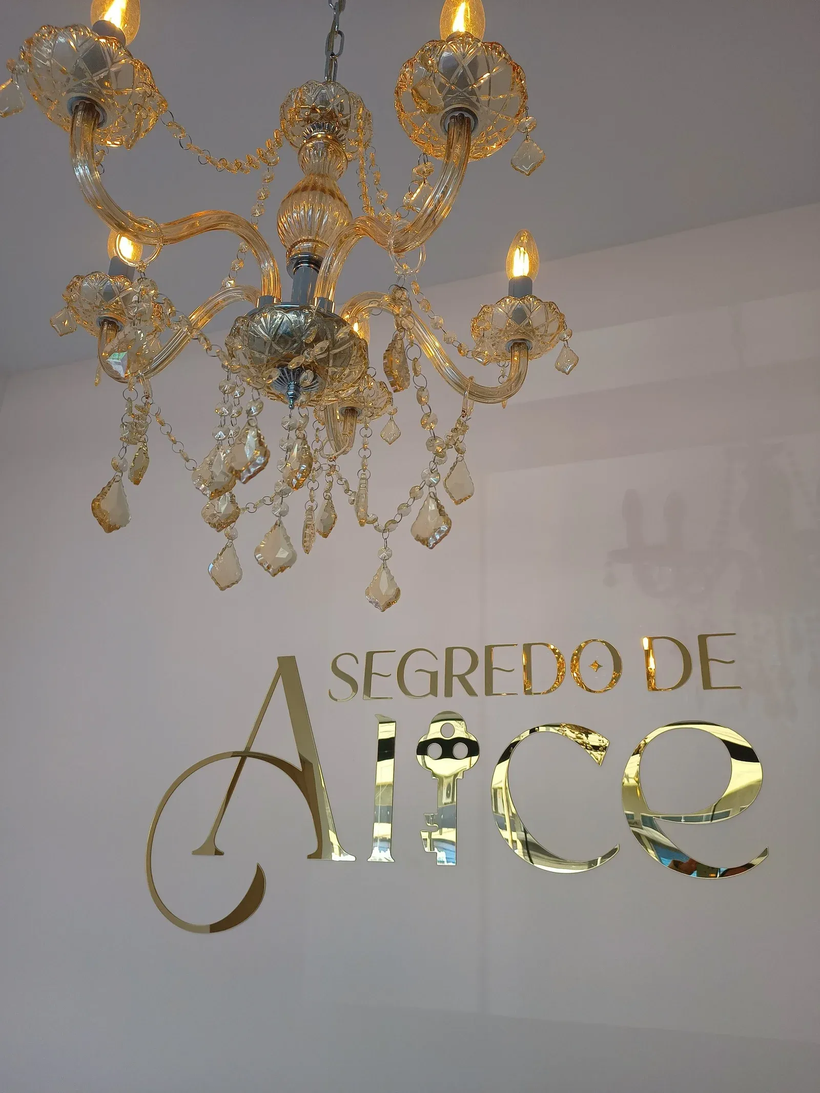 Lustre de cristal sobre o logo dourado na parede